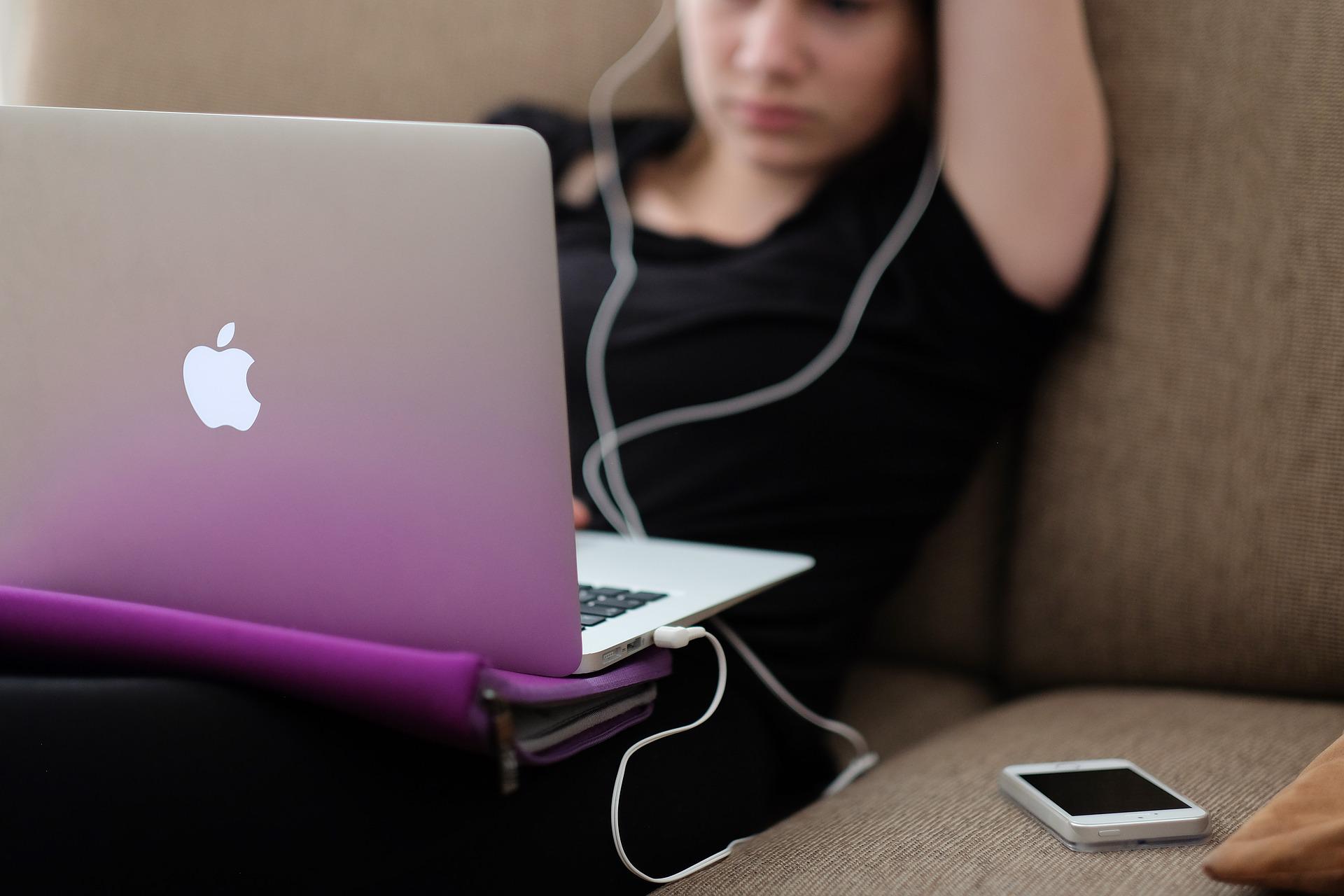 Girl using macbook air with earphones on and smartphone beside her